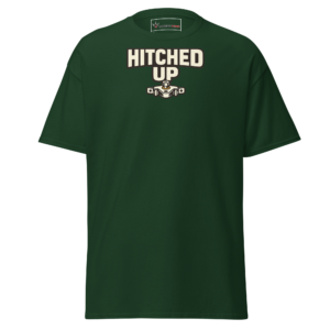 Front view of a forest-green T-Shirt featuring cream “Hitched Up” lettering above a small tractor-and-implement coupling graphic